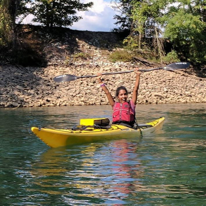 A young woman kayaking holding her paddle up triumphantly.