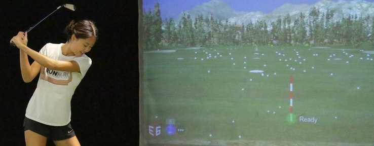 A young woman playing golf using the sport simulator.